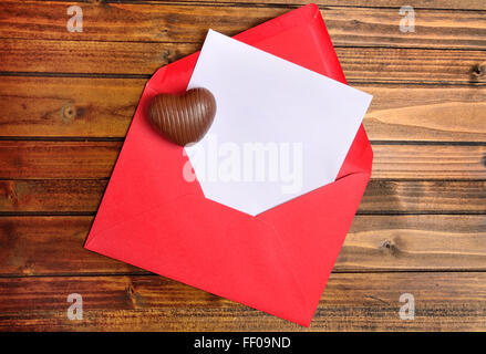 Enveloppe rouge avec du papier blanc et chocolat coeur sur table Banque D'Images