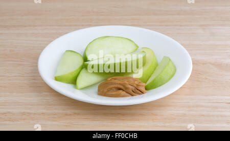 Un groupe de tranches de pomme verte sur un plat avec une petite quantité de beurre d'arachide pour plonger sur un dessus de table en bois Banque D'Images