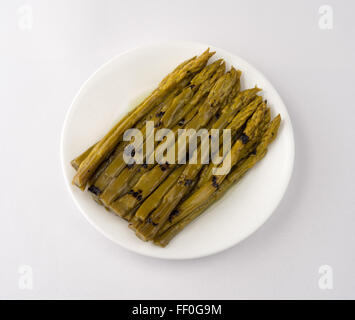 Une portion d'asperges grillées trempées dans l'huile de tournesol sur une plaque blanche au sommet d'une nappe blanche off Banque D'Images