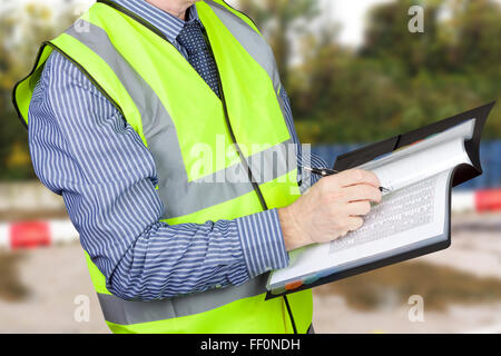 Building surveyor en hi vis de contrôle de données et en prenant des notes dans son dossier de site Banque D'Images