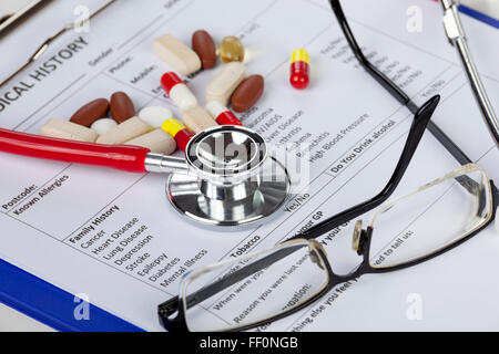 Stéthoscope rouge lunettes et certaines pilules renversé en établissant un formulaire médical sur un presse-papiers Banque D'Images