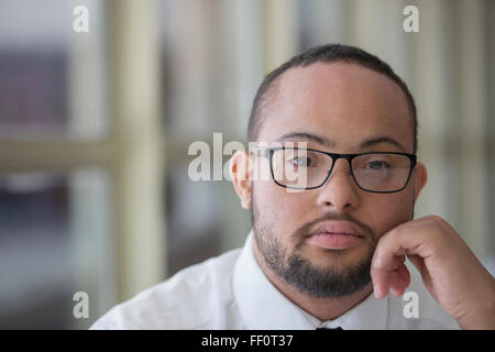 Mixed Race man with down syndrome resting chin en mains Banque D'Images