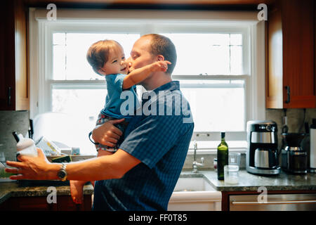 Père embrassant bébé fils dans la cuisine Banque D'Images