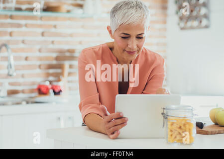 Older Caucasian woman using digital tablet in kitchen