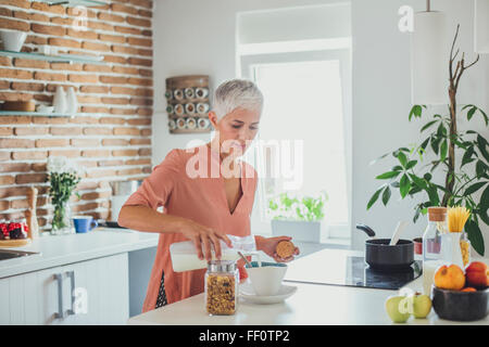 Older Caucasian woman pouring milk in kitchen Banque D'Images