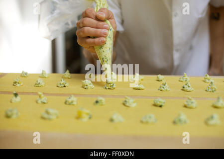 Une vue rapprochée d'un chef d'un remplissage de la tuyauterie des pâtes poche à douille à des feuilles de pâtes maison. Banque D'Images