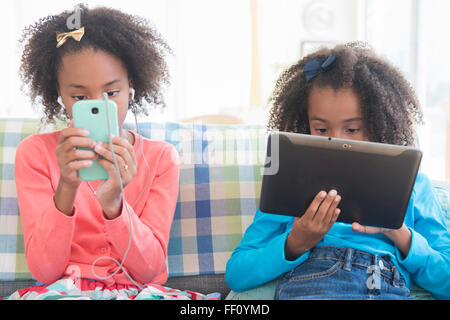 Mixed Race sisters en utilisant la technologie sur canapé Banque D'Images