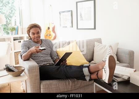 Mixed Race man watching television on sofa Banque D'Images