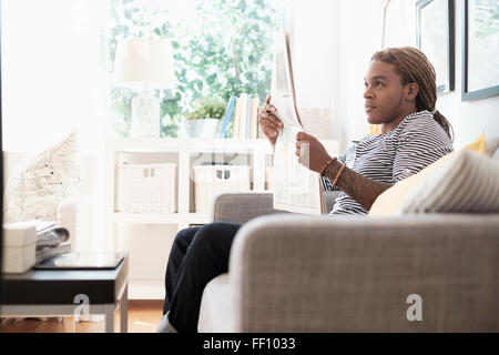 Mixed Race man reading newspaper on sofa Banque D'Images