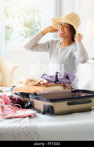 Mixed Race woman packing suitcase in bed Banque D'Images