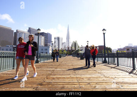 Les gens qui marchent le long du quai 7 sur une journée ensoleillée sur l'Embarcadero de San Francisco avec la Transamerica Pyramid en arrière-plan. Banque D'Images