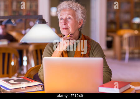 Plus mixed race woman using laptop in library Banque D'Images