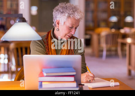 Plus mixed race woman using laptop in library Banque D'Images