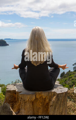 Older Caucasian woman meditating on cliff près de ocean Banque D'Images