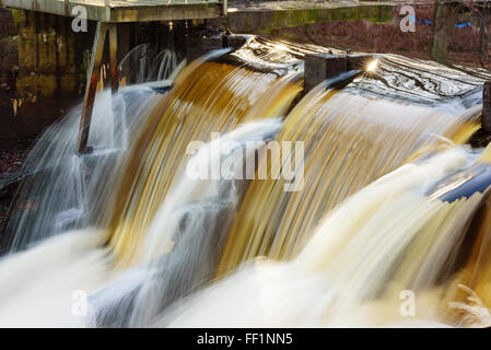 En cascade de l'eau sur le bord d'un petit barrage. L'eau est riche en minéraux et brunâtre. Barrage a petits trous sur le côté que la fuite. Banque D'Images