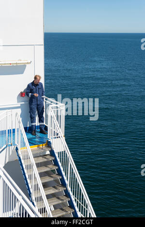 Machiniste marin en bleu sur l'ensemble des vêtements de travail fumeurs pendant escalier pause cigarette au soleil avec la mer Baltique Banque D'Images