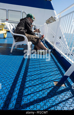 Transport des passagers sur le pont supérieur au soleil assis sur des chaises à la recherche sur smartphone sur voyage sur la mer Baltique à la Suède Banque D'Images