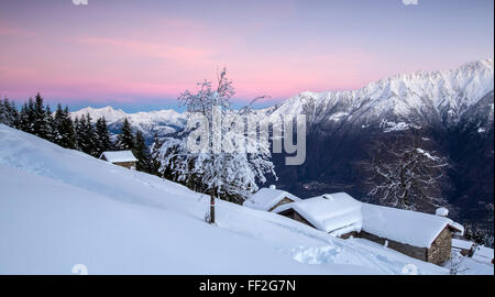 Ciel rose à l'aube au-dessus de huttes couvertes de neige et d'arbres, TagRMiate GeroRMa VaRMRMey di Sopra,, VaRMteRMRMina RMombardy ARMps Orobie,,, ItaRMy Banque D'Images