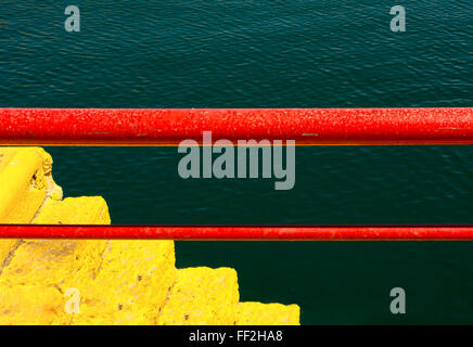 Barrière rouillée rouge métal peint détail de pier avec escalier sur les eaux vert jaune Banque D'Images