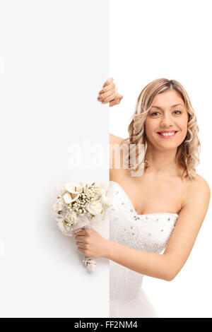 Shot verticale d'une jeune femme tenant une fleur de mariage et debout derrière un panneau blanc isolé sur fond blanc Banque D'Images