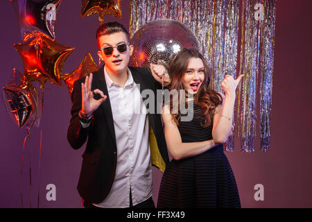 Beau jeune couple having party et showing Thumbs up et ok sur fond violet Banque D'Images