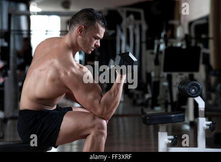 Puissance très sportif bodybuilder exécuter l'exercice avec haltères en sport sombre Banque D'Images