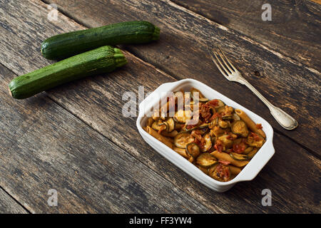 Des pâtes alimentaires de blé entier avec les courgettes dans un plat allant au four de blanc et de la vieille table en bois Banque D'Images