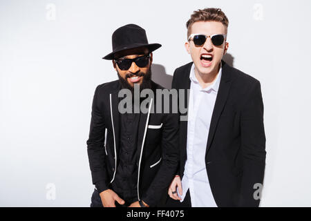 Deux jeunes hommes modernes irritée en costumes noirs et criant à la caméra à over white background Banque D'Images