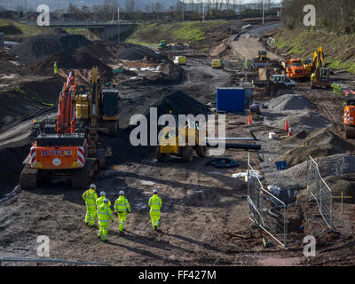 La construction de nouvelles routes site, montrant les hommes qui travaillent dans l'équipement de sécurité, les excavatrices et camions à benne. Banque D'Images