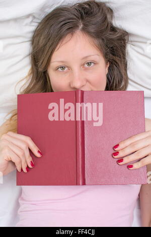 Jeune fille endormie dans un lit de pose avec un livre dans ses mains Banque D'Images