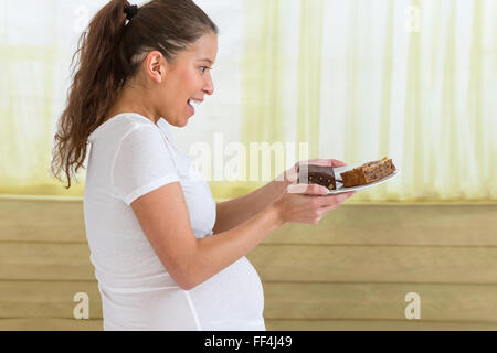 Young pregnant woman eating gâteau sucré à la maison Banque D'Images