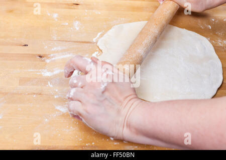 Femme de rouleaux sur la pâte avec un rouleau à pâtisserie sur la table en bois Banque D'Images
