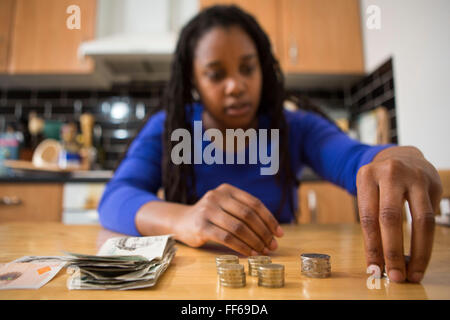 Une jeune femme est assise à sa table de cuisine en comptant son argent pour payer les factures du ménage. Banque D'Images