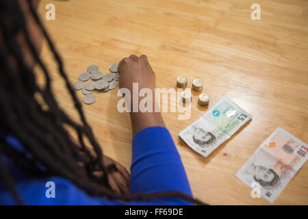 Une jeune femme est assise à sa table de cuisine en comptant son argent pour payer les factures du ménage. Banque D'Images