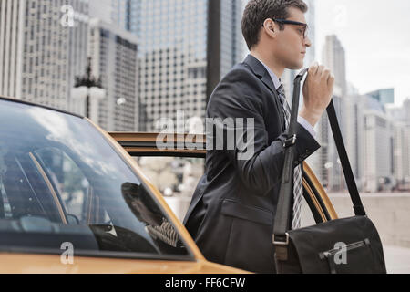 Une journée de travail. Un homme d'affaires en costume et cravate de travail avec un sac d'ordinateur en sortant d'un taxi. Banque D'Images