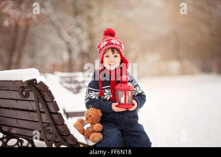 Adorable petit garçon caucasien avec ours et lanterne rouge, jouant dans le parc d'hiver, jour de neige Banque D'Images