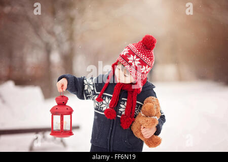 Adorable petit garçon caucasien avec ours et lanterne rouge, jouant dans le parc d'hiver, jour de neige Banque D'Images