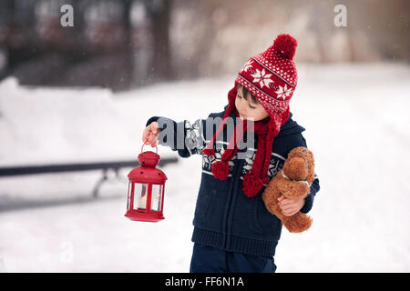 Adorable petit garçon caucasien avec ours et lanterne rouge, jouant dans le parc d'hiver, jour de neige Banque D'Images