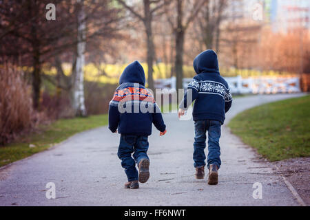 Deux garçons doux en fuite sur un sentier dans le parc dans le cadre d'une journée d'hiver ensoleillée, l'activité en plein air Banque D'Images