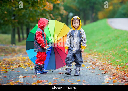 Deux adorables enfants, frères, Garçon jouant dans parc avec parapluie arc-en-ciel de couleurs sur un jour d'automne pluvieux Banque D'Images