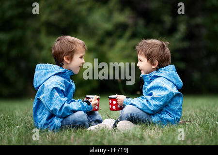 Deux beaux garçons, frères, assis sur une pelouse, temps d'automne, boire du thé et manger des biscuits dans le park Banque D'Images