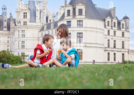 Deux adorables garçons et maman de vêtements, la consommation de crème glacée assis sur une pelouse en face de la plus grand château le long de la Loire Banque D'Images