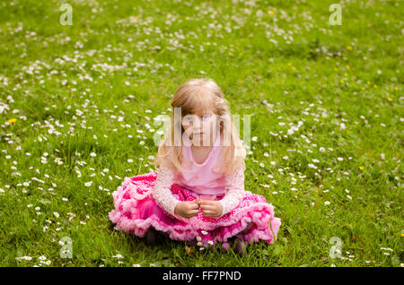 Belle blonde girl sitting in green meadow with white daisies Banque D'Images