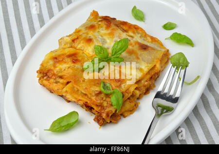 Avec des feuilles de basilic lasagne délicieux servi sur une assiette avec une fourchette à côté Banque D'Images