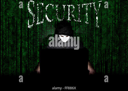 Un homme masqué à un ordinateur portable symbolisant les dangers de l'Internet. Banque D'Images