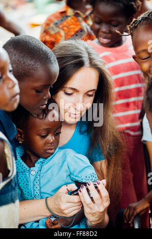 Le Mali, l'Afrique. Jeune femme de race blanche entourée d'enfants noirs en regardant un smartphone près de Bamako Banque D'Images