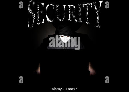 Un homme masqué à un ordinateur portable symbolisant les dangers de l'Internet. Banque D'Images