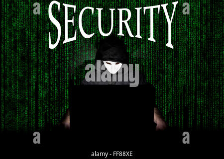 Un homme masqué à un ordinateur portable symbolisant les dangers de l'Internet. Banque D'Images