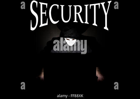 Un homme masqué à un ordinateur portable symbolisant les dangers de l'Internet. Banque D'Images