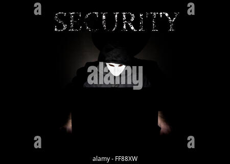 Un homme masqué à un ordinateur portable symbolisant les dangers de l'Internet. Banque D'Images